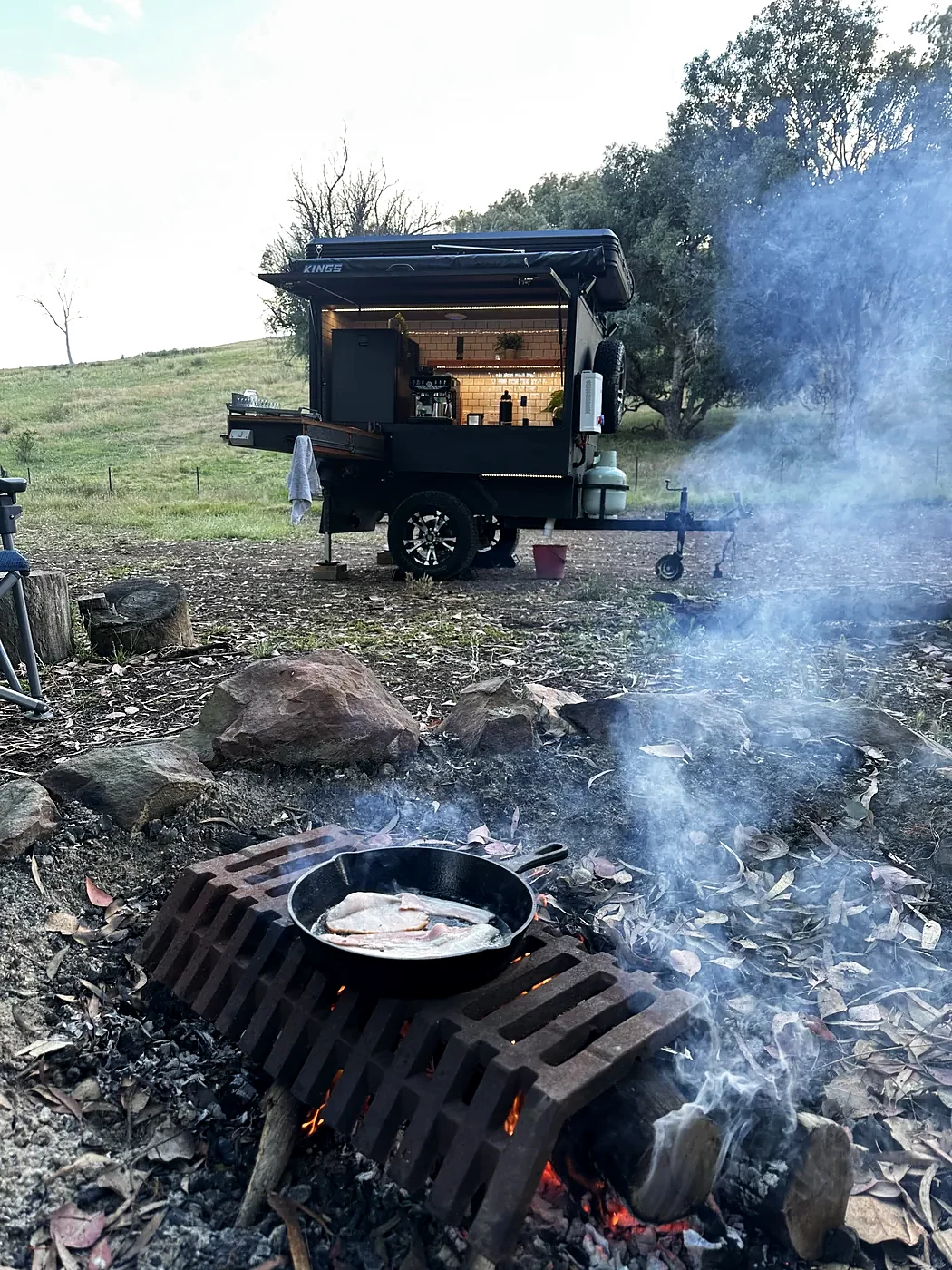 Camper at dusk with the kitchen open and a campfire