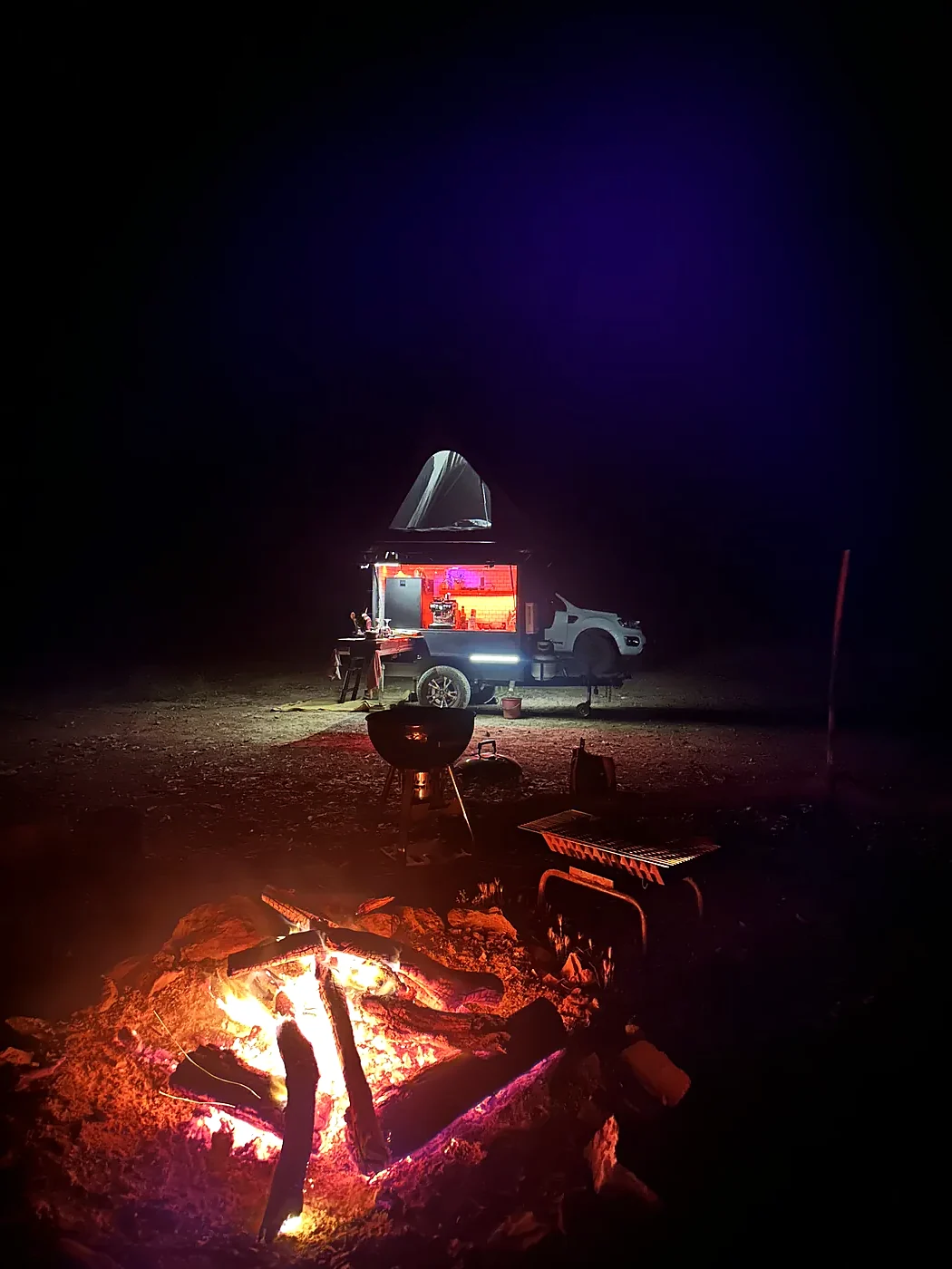 Camper and rooftop tent lit at a dark campsite