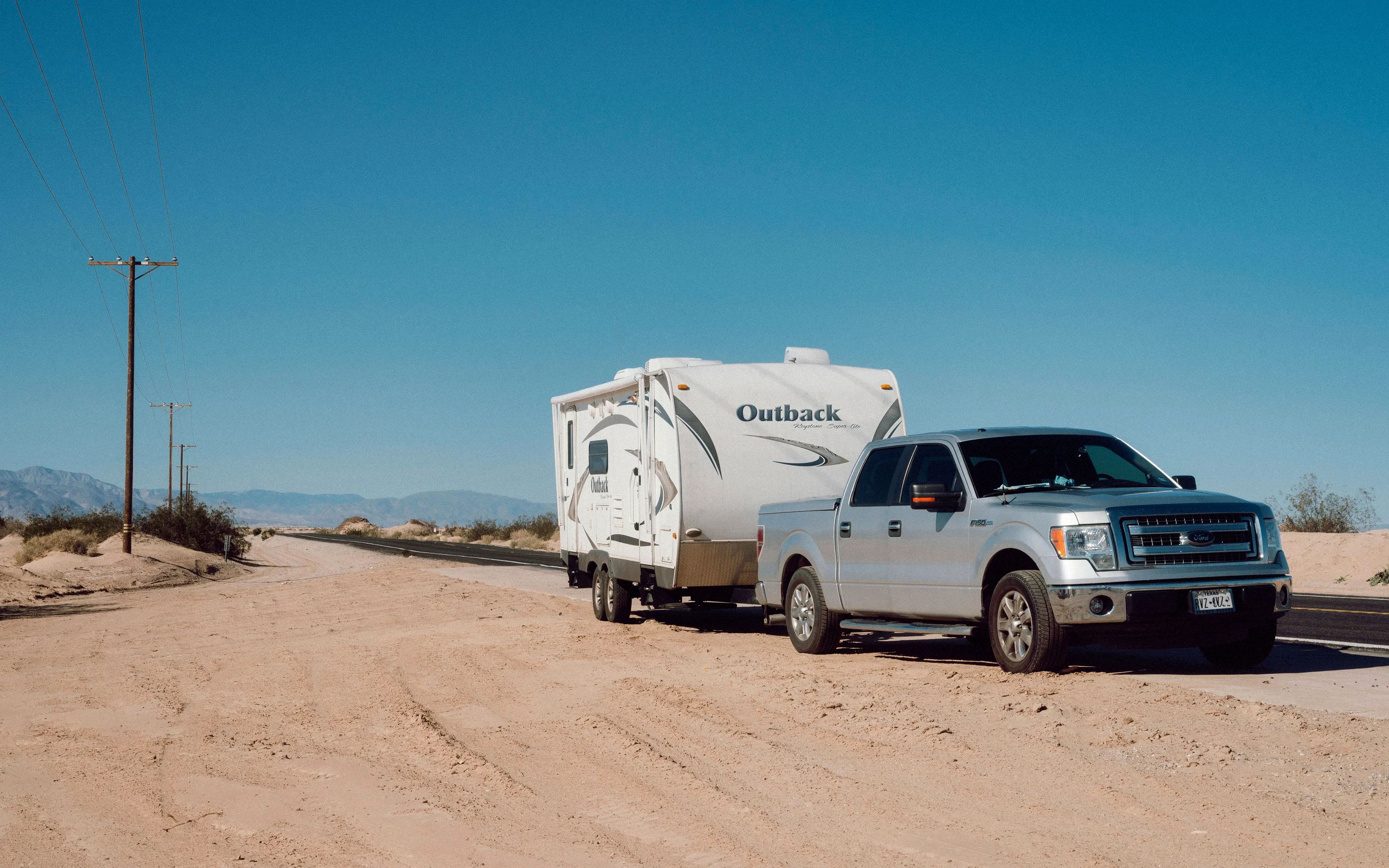 Silver pickup towing a modern Outback travel trailer on a desert highway