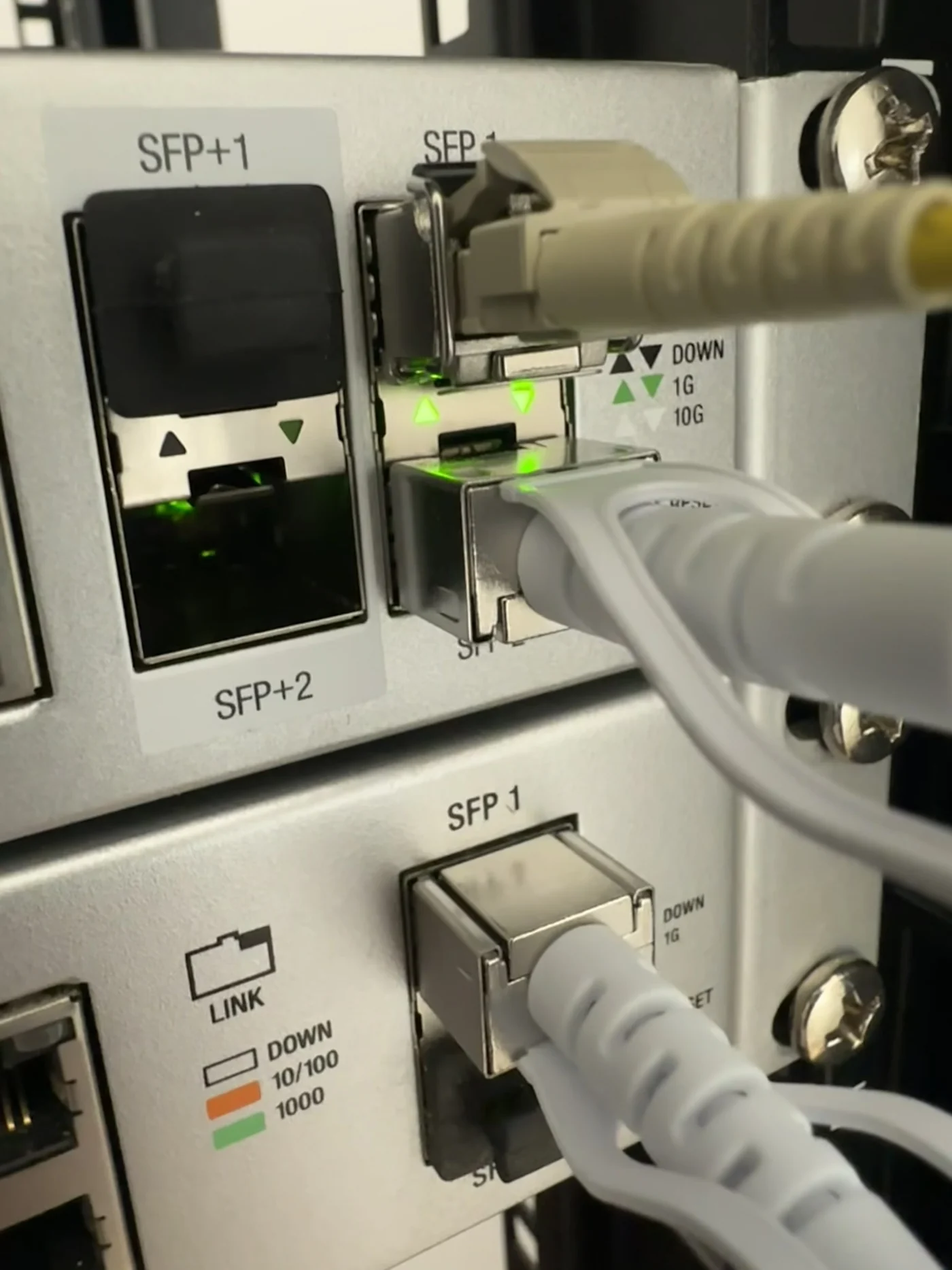 Close-up of rack network switch with live SFP+ fibre and white patch cables, green link LEDs on